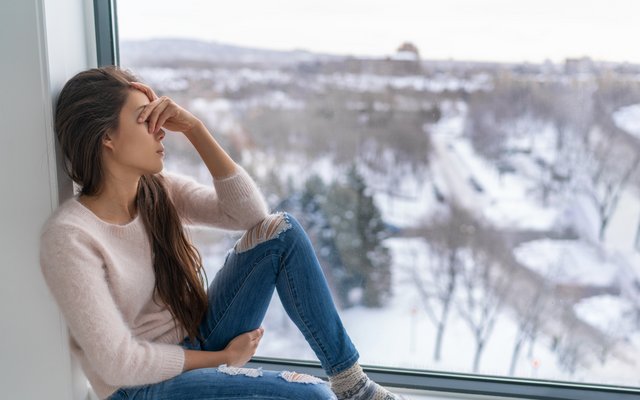 traurige Frau sitzt am Fenster und schaut in die kalte Winterlandschaft