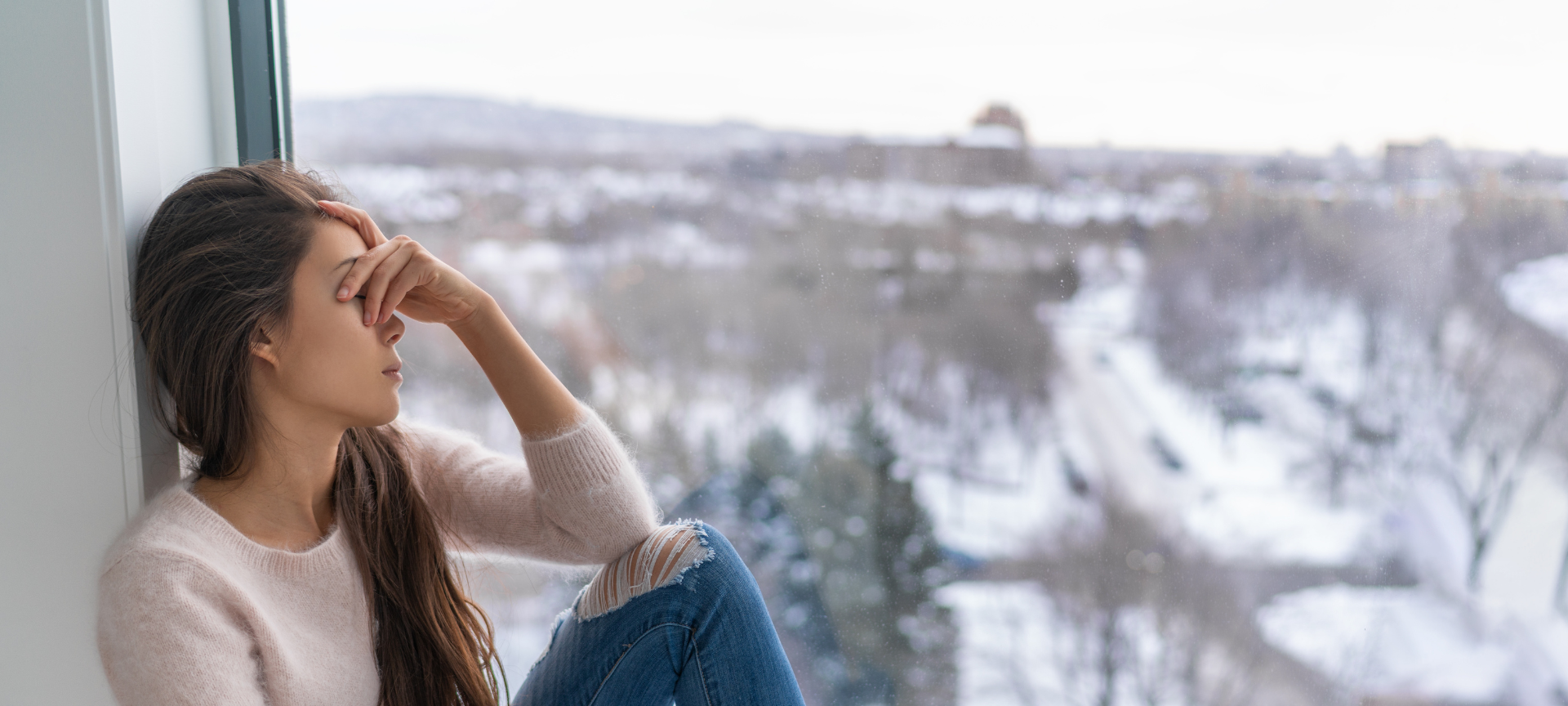 traurige Frau sitzt am Fenster und schaut in die kalte Winterlandschaft